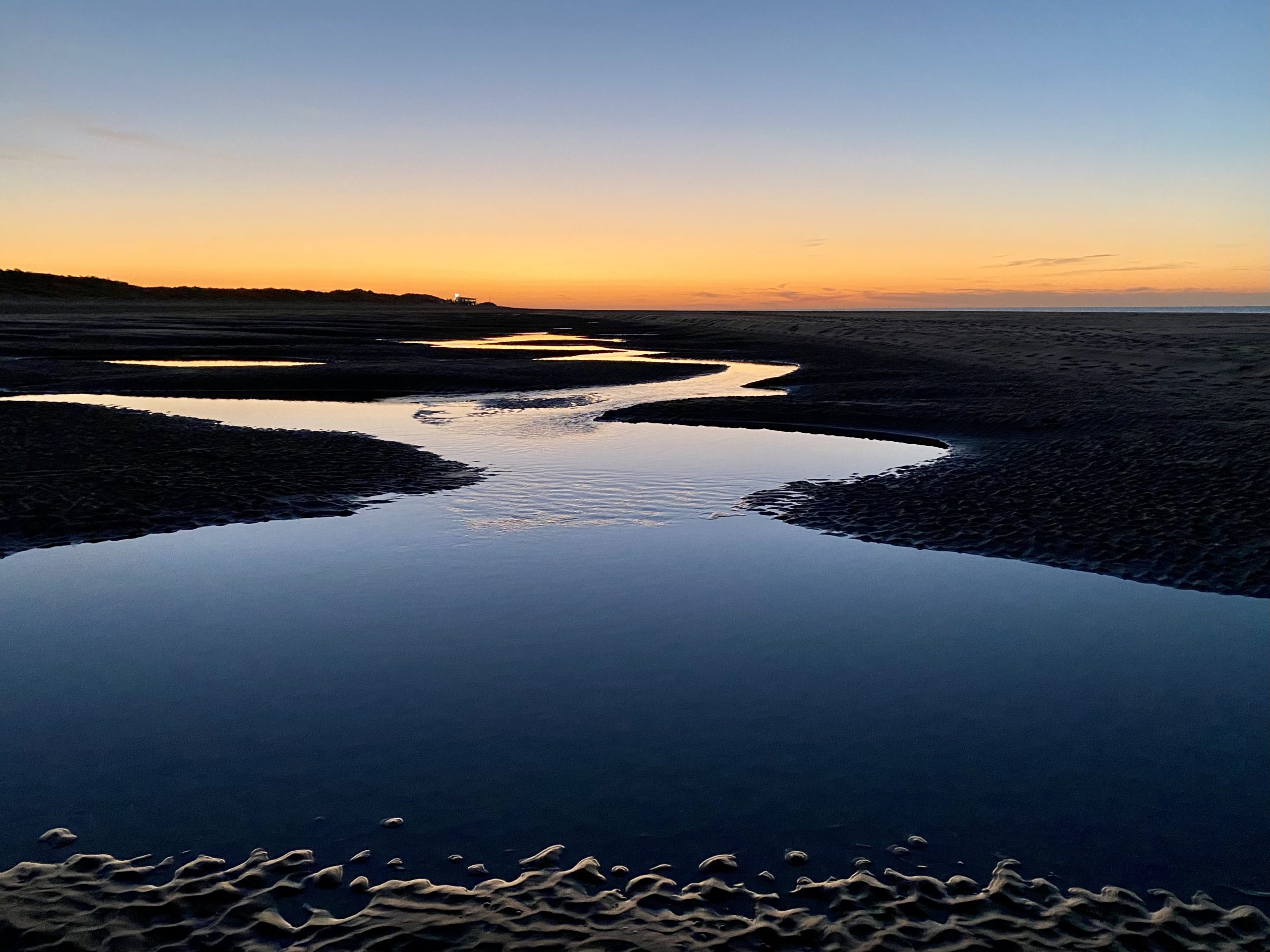 Sonnenuntergang über einer ruhigen, geschwungenen Wasserlandschaft am Strand – Sinnbild für Klarheit, Tiefe und sanfte Führung.
